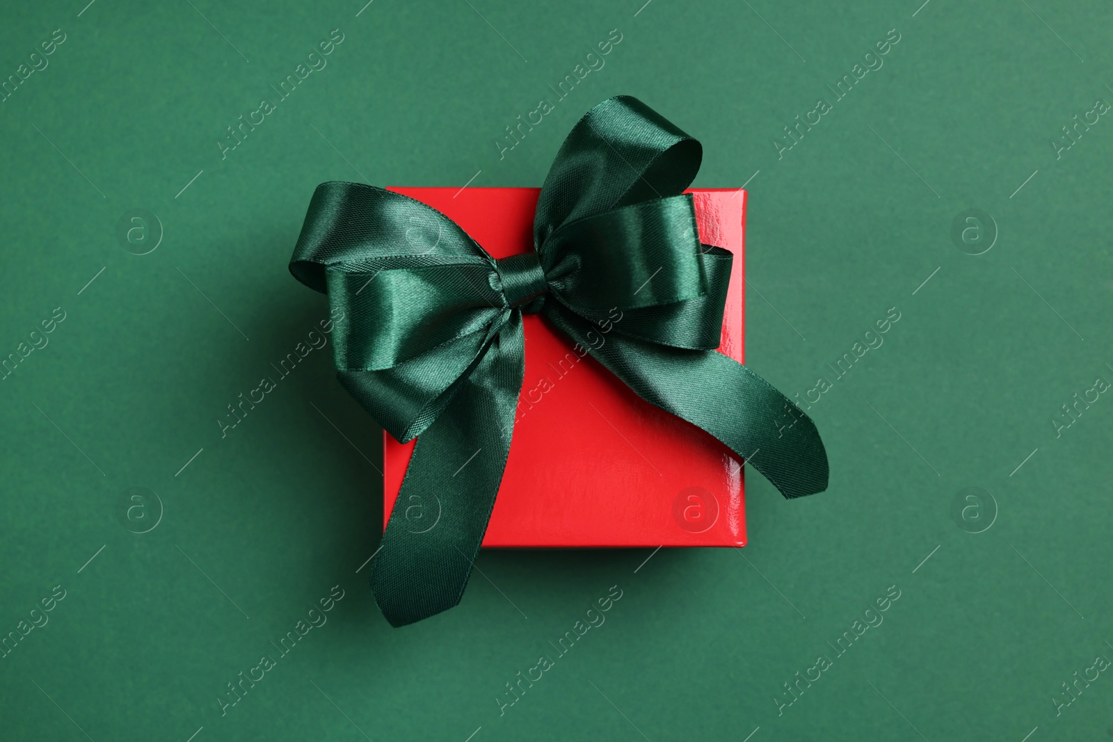 Photo of Beautiful red gift box with bright bow on green background, top view