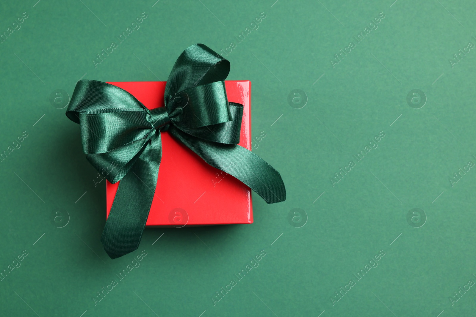 Photo of Beautiful red gift box with bright bow on green background, top view. Space for text