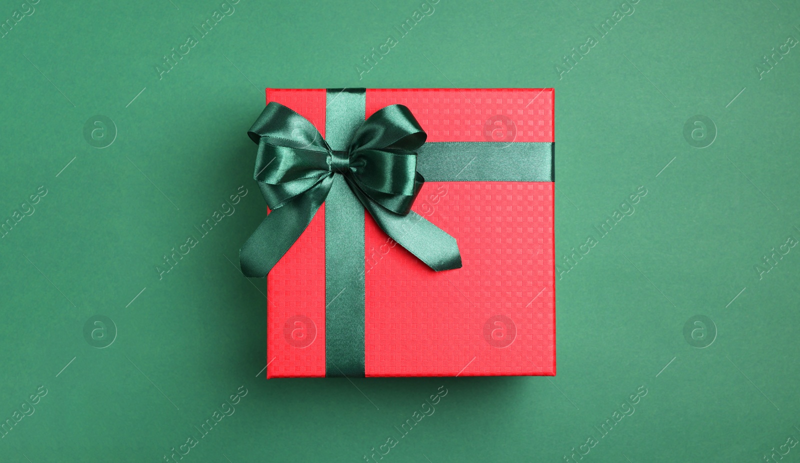 Photo of Beautiful red gift box with bright bow on green background, top view. Space for text