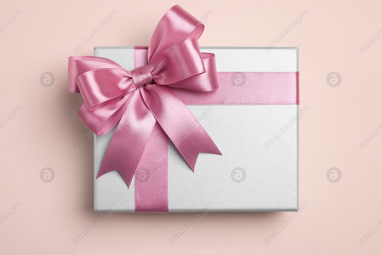 Photo of Beautiful gift box with pink bow on beige background, top view