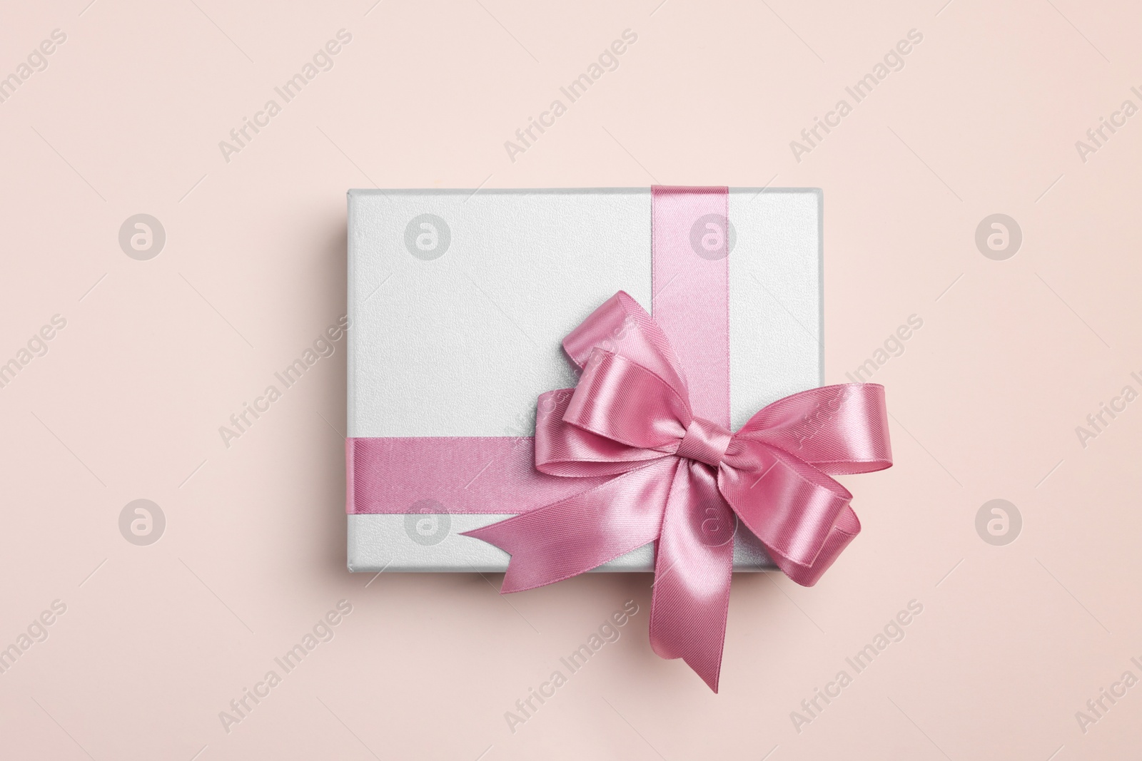 Photo of Beautiful gift box with pink bow on beige background, top view