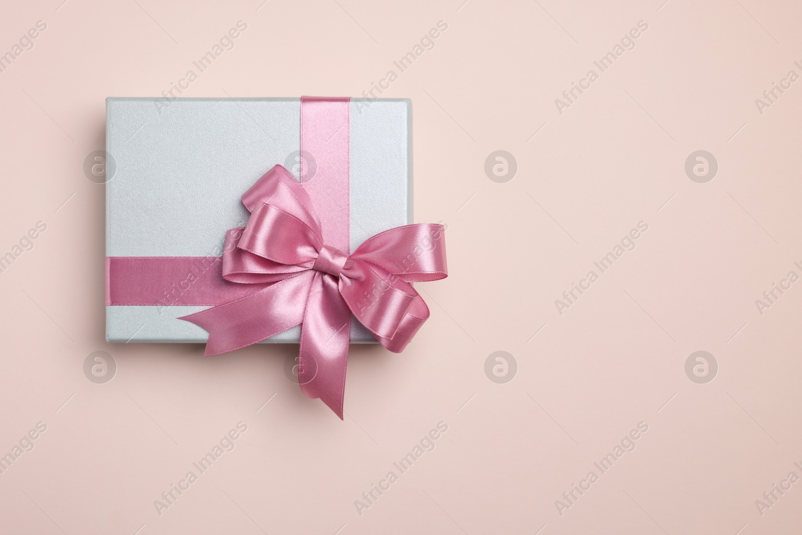 Photo of Beautiful gift box with pink bow on beige background, top view. Space for text