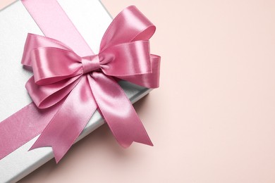 Photo of Beautiful gift box with pink bow on beige background, top view. Space for text