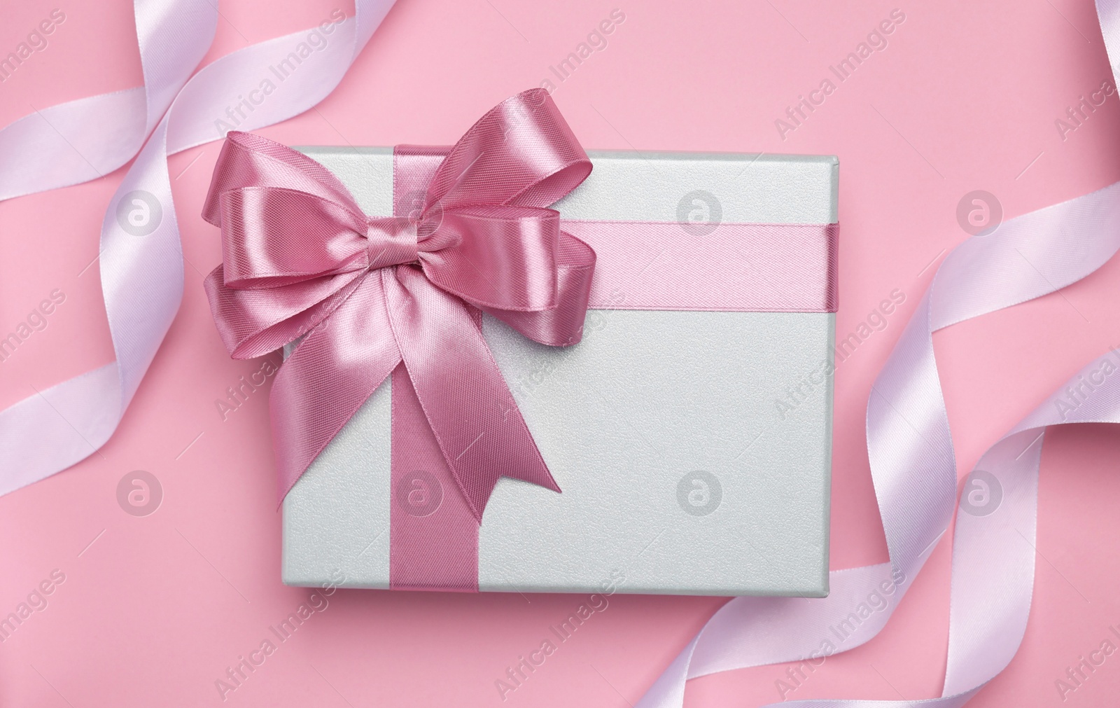 Photo of Beautiful gift box with color bow and ribbons on pink background, flat lay