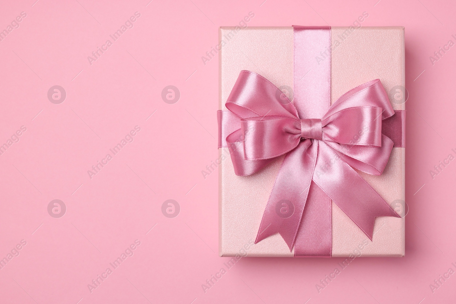 Photo of Beautiful gift box with color bow on pink background, top view. Space for text