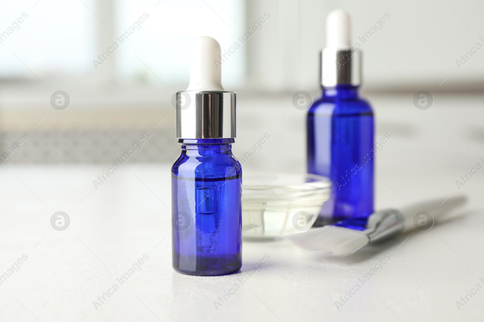 Photo of Peeling procedure. Bottles of chemical peel, bowl with liquid and brush on white table indoors