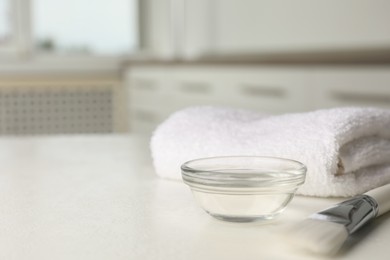 Photo of Peeling procedure. Chemical peel liquid in bowl, brush and towel on white table indoors. Space for text