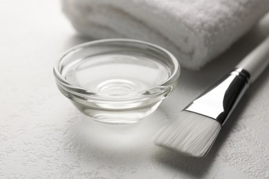 Photo of Peeling procedure. Chemical peel liquid in bowl, towel and brush on white table, closeup