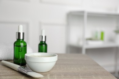 Photo of Peeling procedure. Bottles of chemical peel, bowl with liquid and brush on wooden table indoors. Space for text