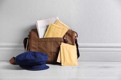 Brown postman's bag, envelopes, newspapers and hat near grey wall. Space for text