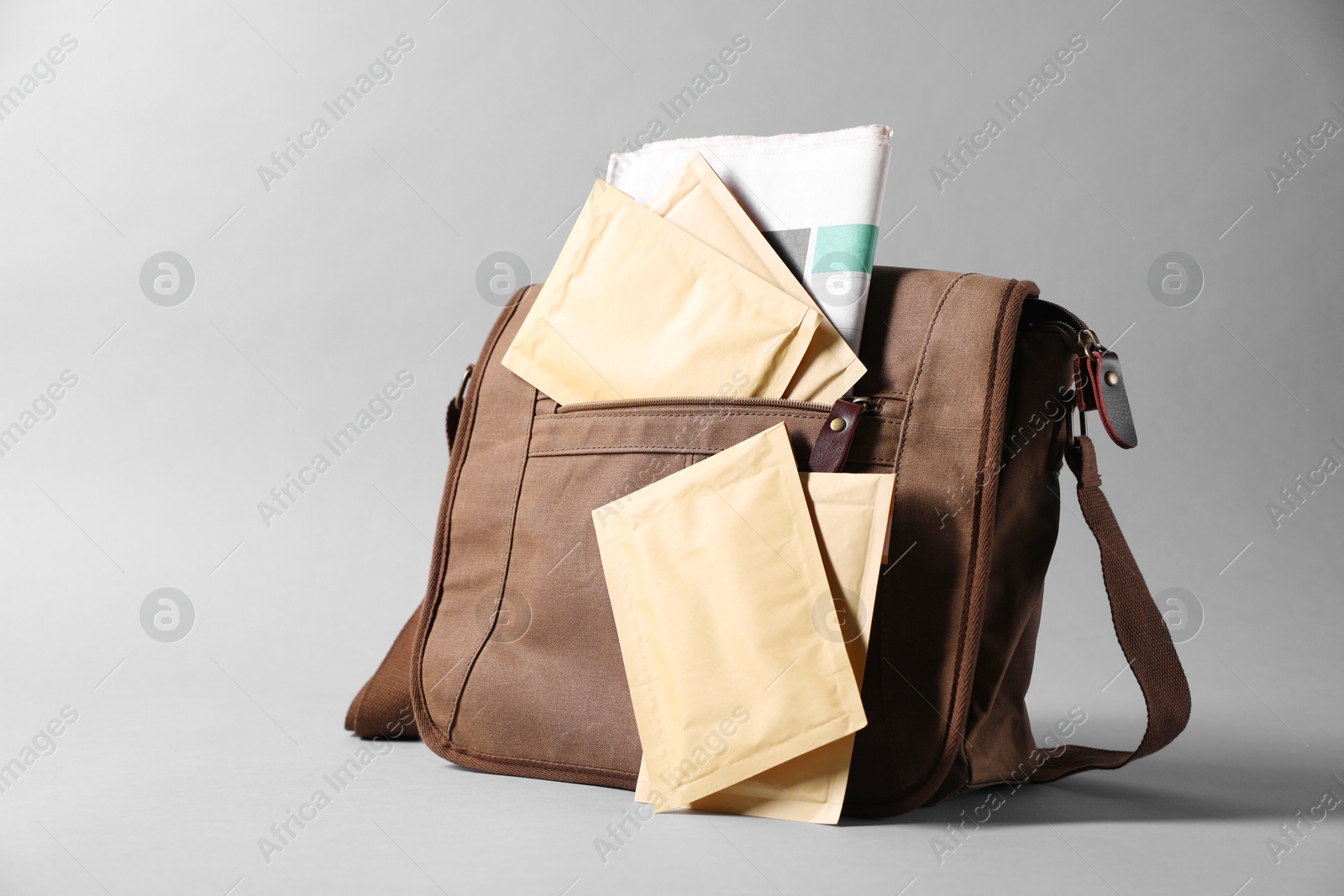 Photo of Brown postman's bag with envelopes and newspapers on grey background