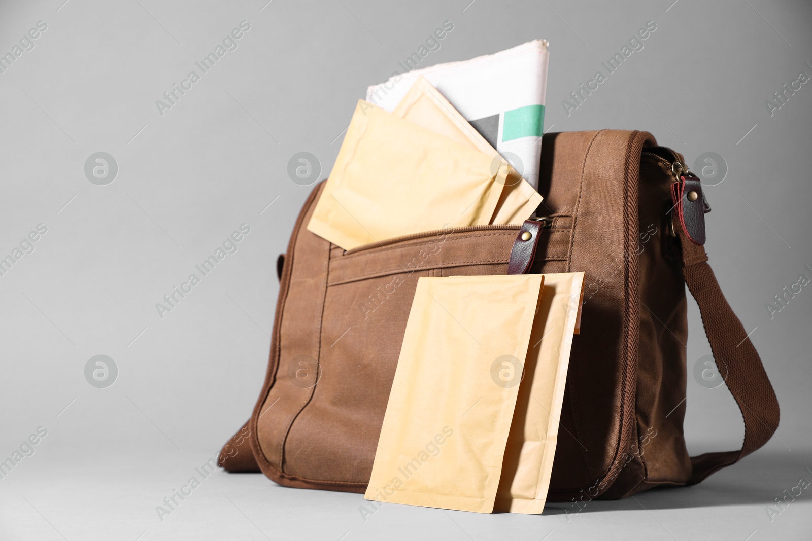 Photo of Brown postman's bag with envelopes and newspapers on grey background