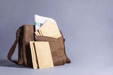 Brown postman's bag with envelopes and newspapers on grey background. Space for text