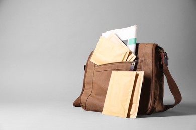 Photo of Brown postman's bag with envelopes and newspapers on grey background. Space for text