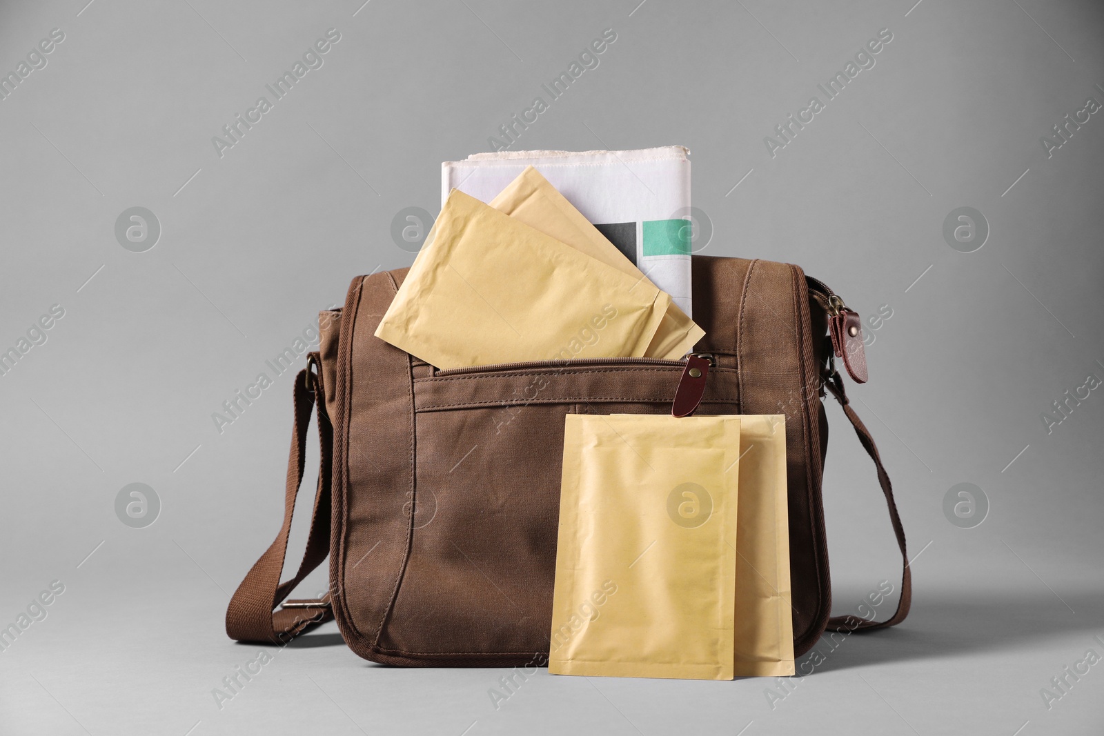 Photo of Brown postman's bag with envelopes and newspapers on grey background