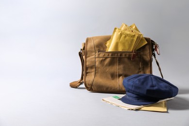 Brown postman's bag, envelopes, newspapers and hat on grey background. Space for text