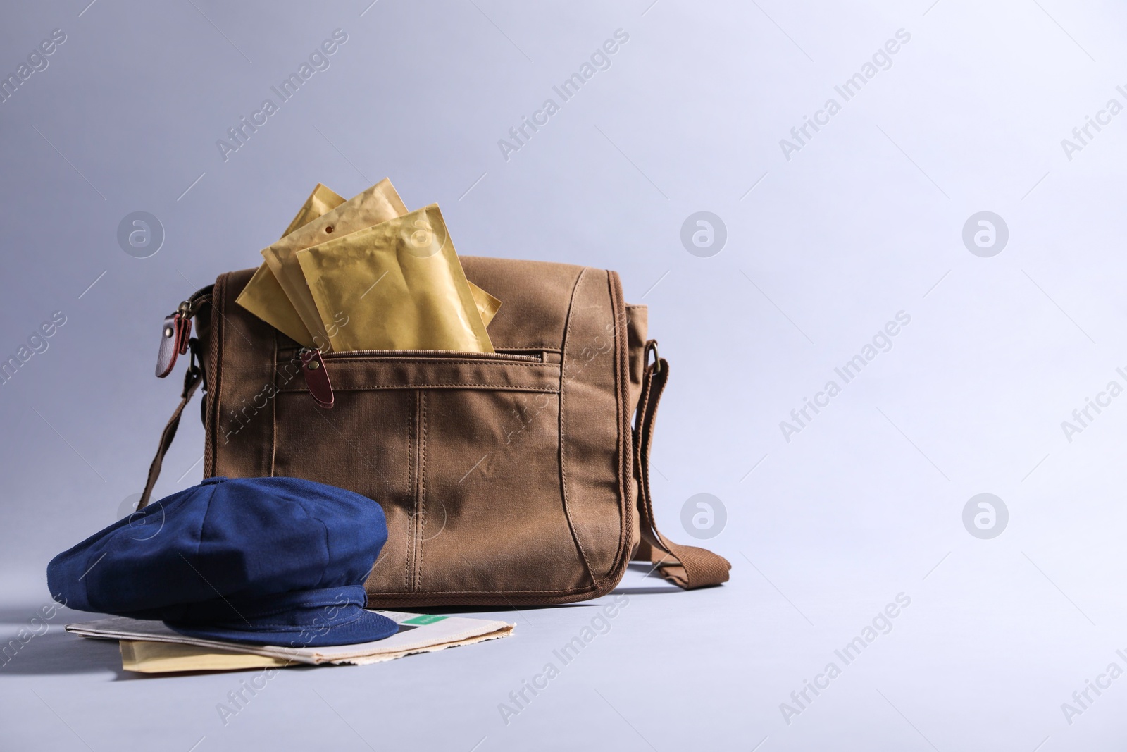 Photo of Brown postman's bag, envelopes, newspapers and hat on grey background. Space for text