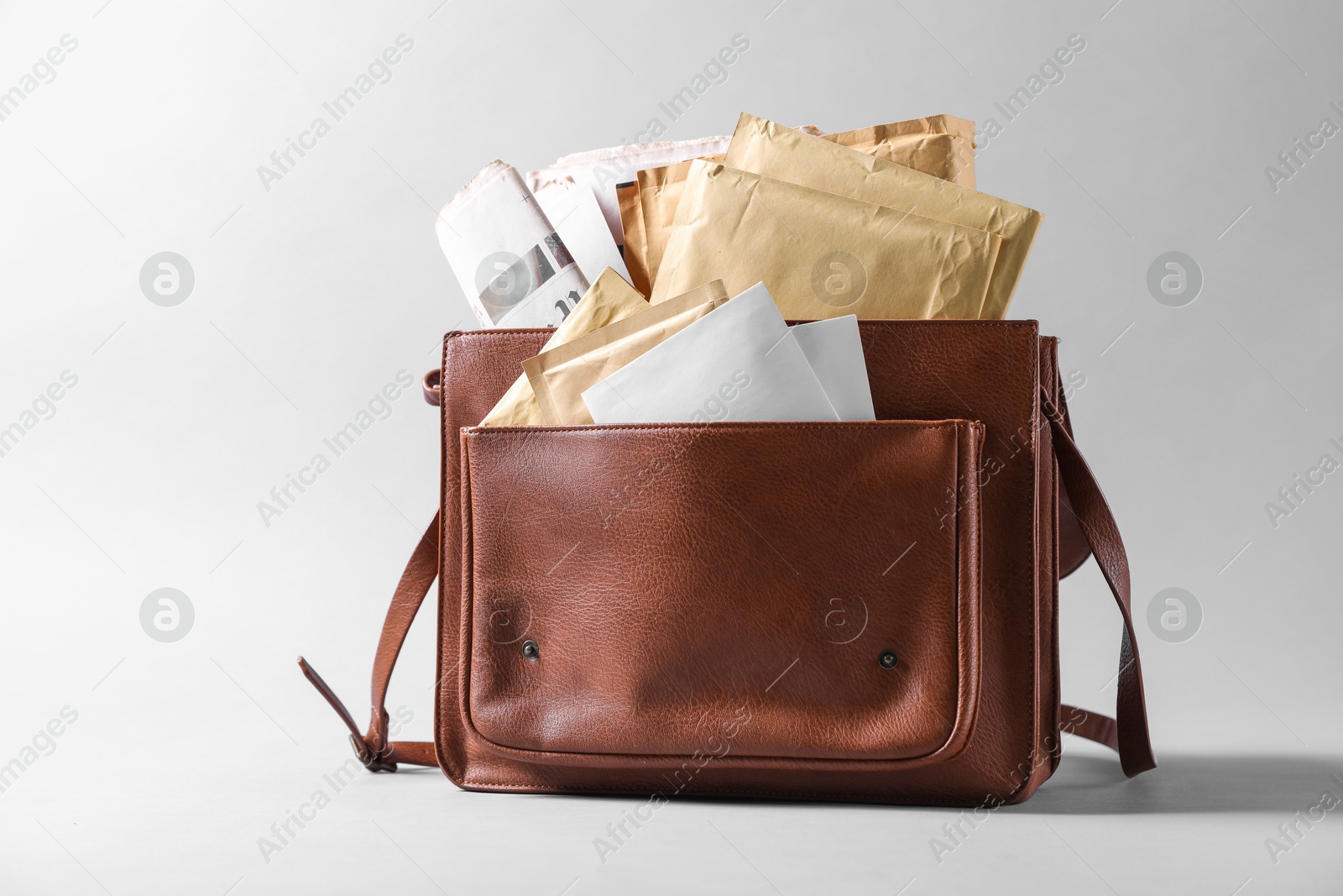 Photo of Brown postman's bag with envelopes and newspapers on grey background