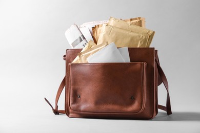 Brown postman's bag with envelopes and newspapers on grey background