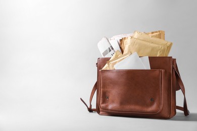 Photo of Brown postman's bag with envelopes and newspapers on grey background. Space for text