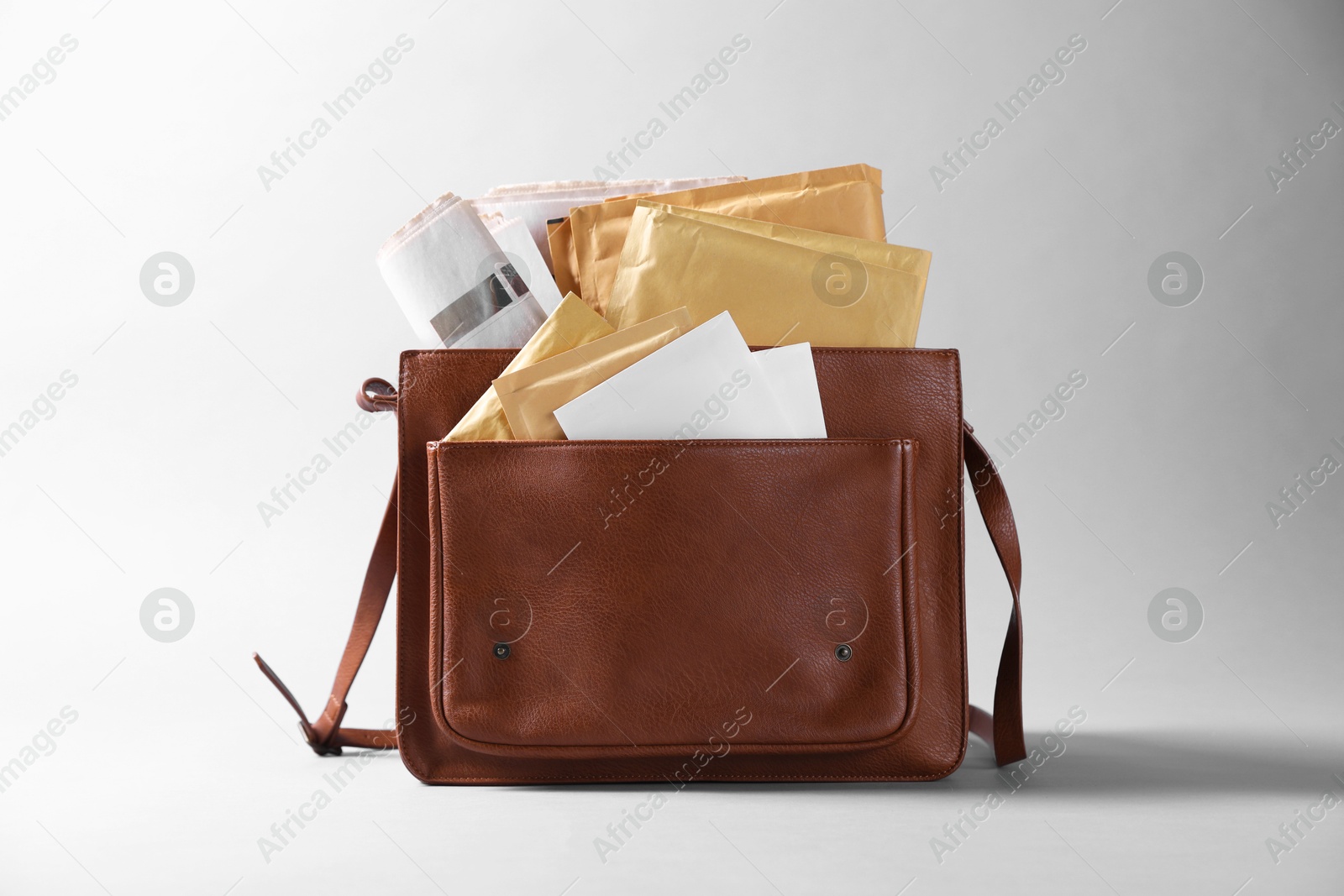 Photo of Brown postman's bag with envelopes and newspapers on grey background