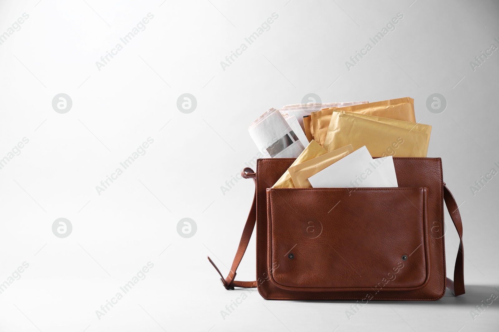 Photo of Brown postman's bag with envelopes and newspapers on grey background. Space for text