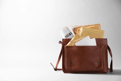 Brown postman's bag with envelopes and newspapers on grey background. Space for text