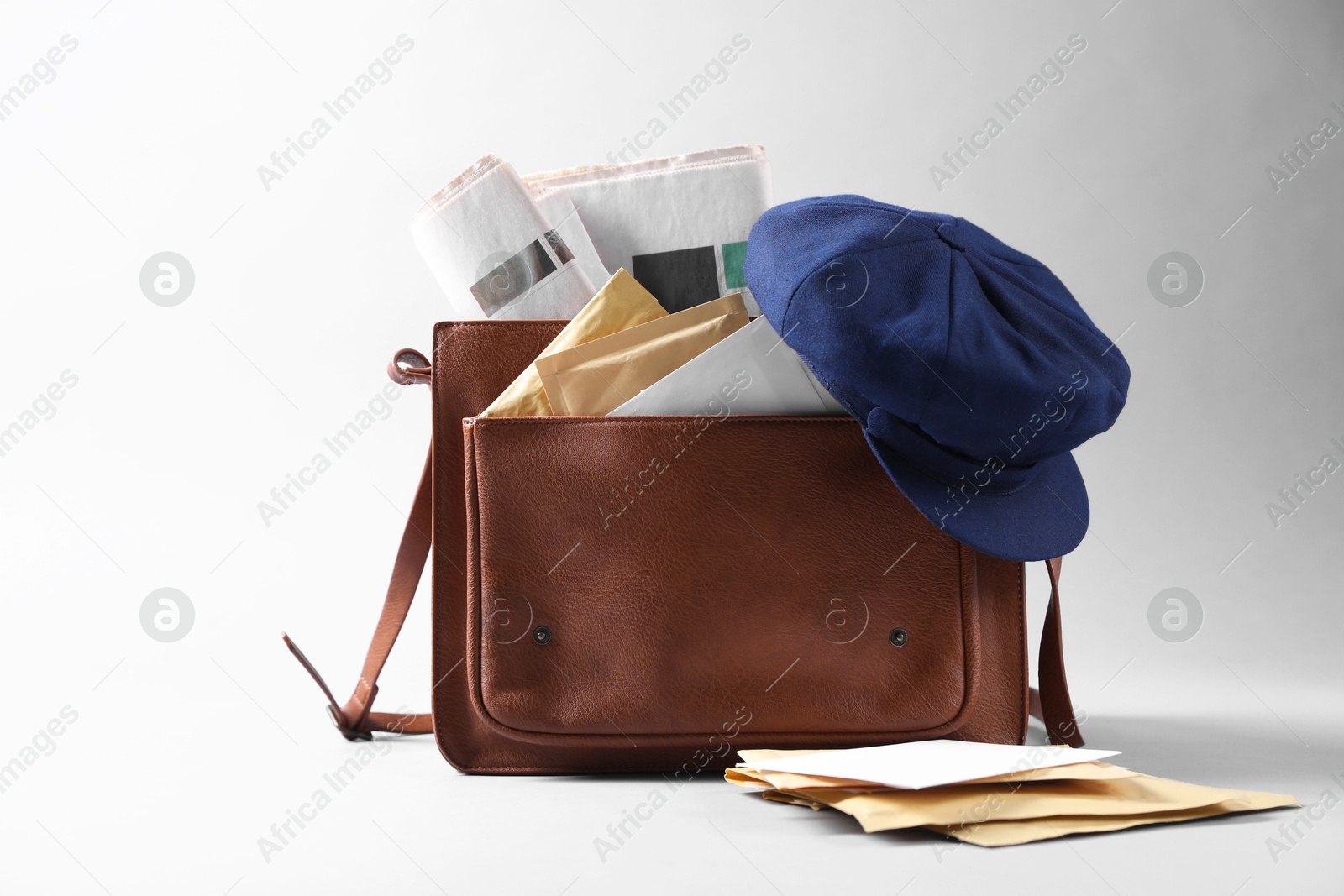 Photo of Brown postman's bag, envelopes, newspapers and hat on grey background