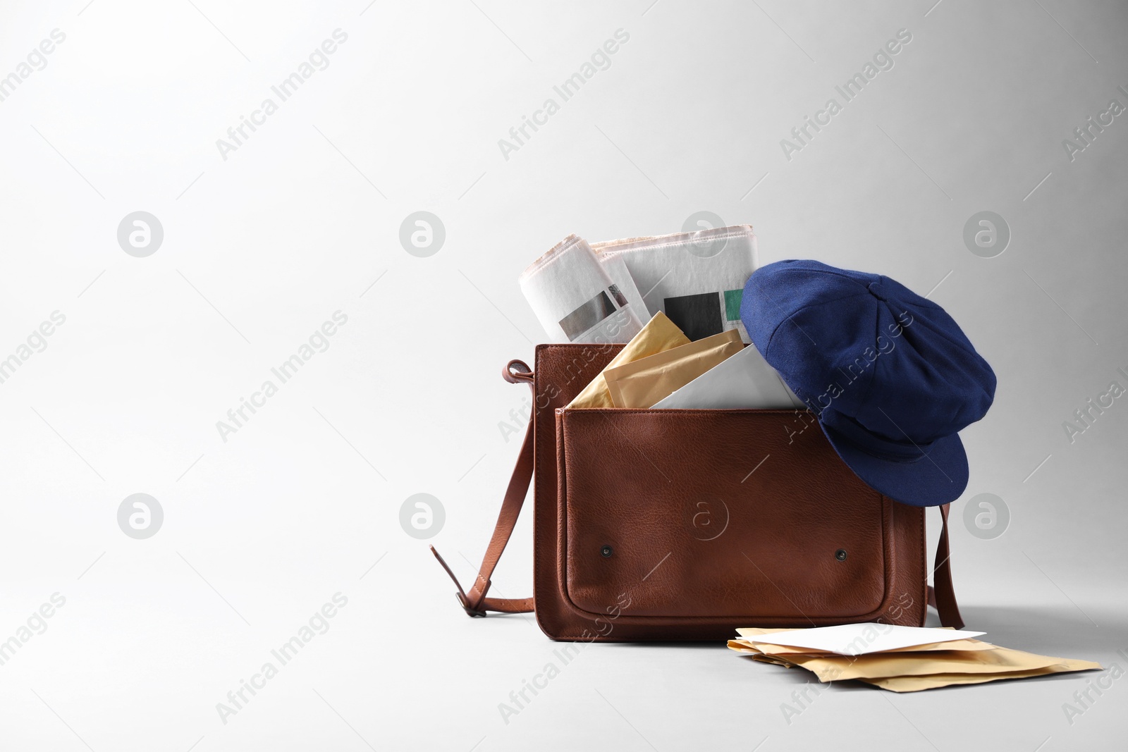 Photo of Brown postman's bag, envelopes, newspapers and hat on grey background. Space for text