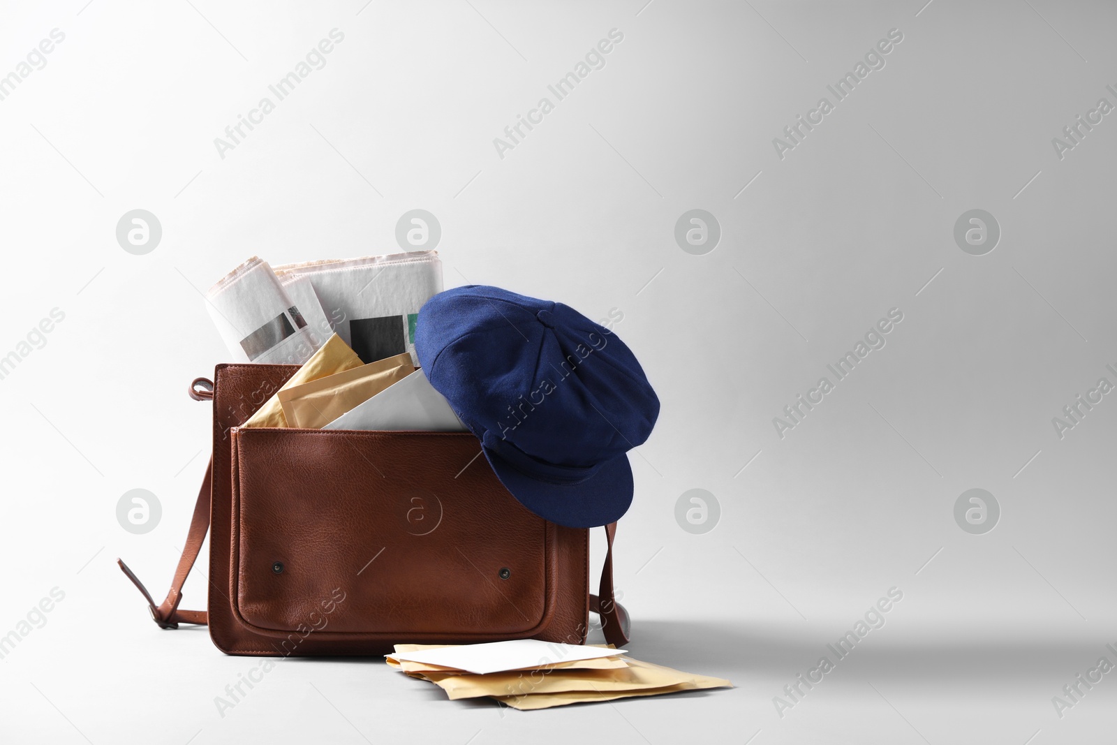 Photo of Brown postman's bag, envelopes, newspapers and hat on grey background. Space for text