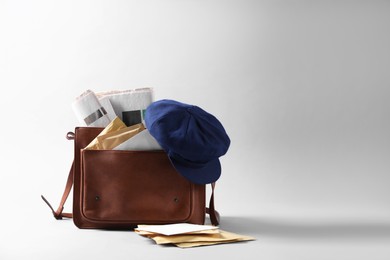 Brown postman's bag, envelopes, newspapers and hat on grey background. Space for text