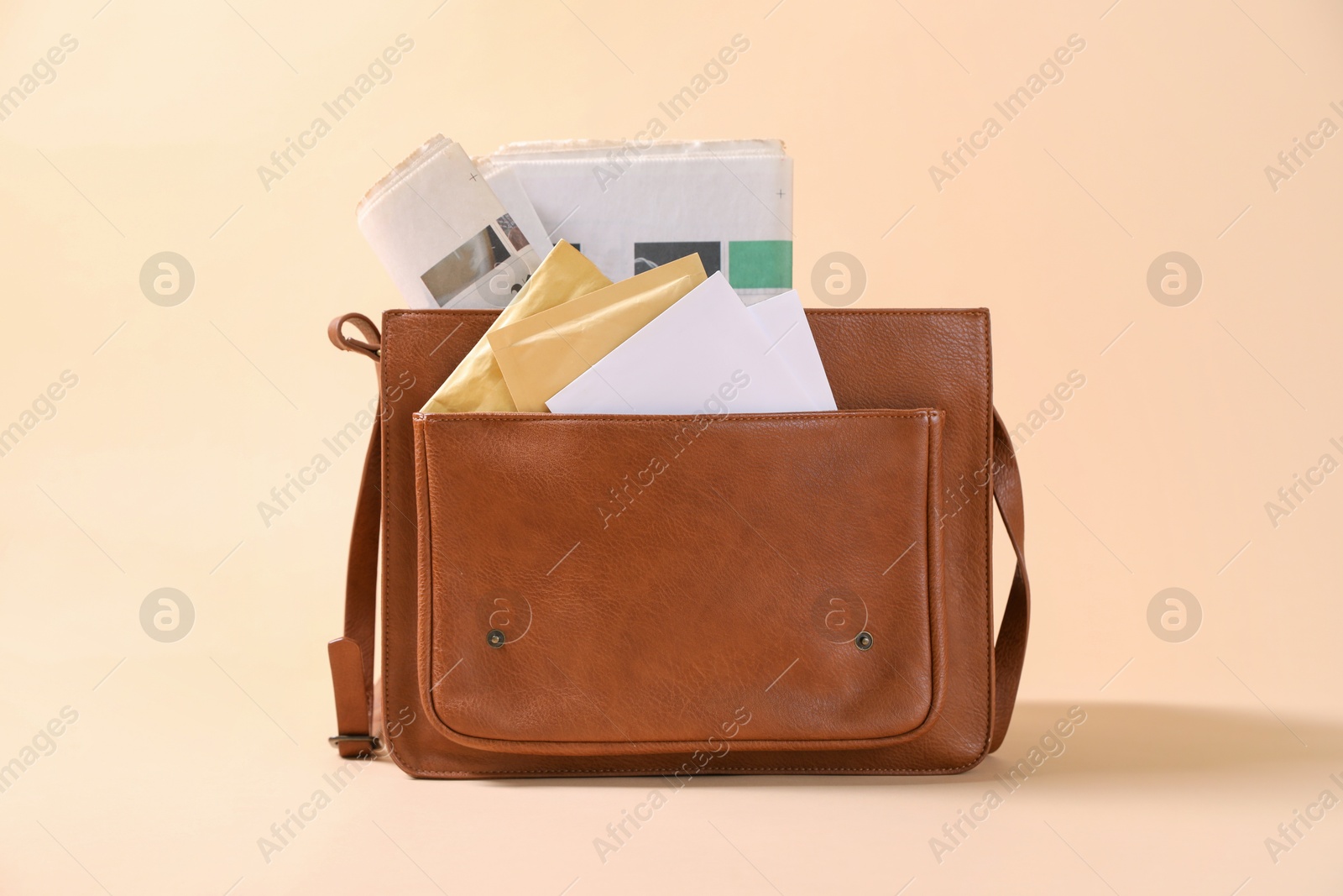 Photo of Brown postman's bag with envelopes and newspapers on beige background