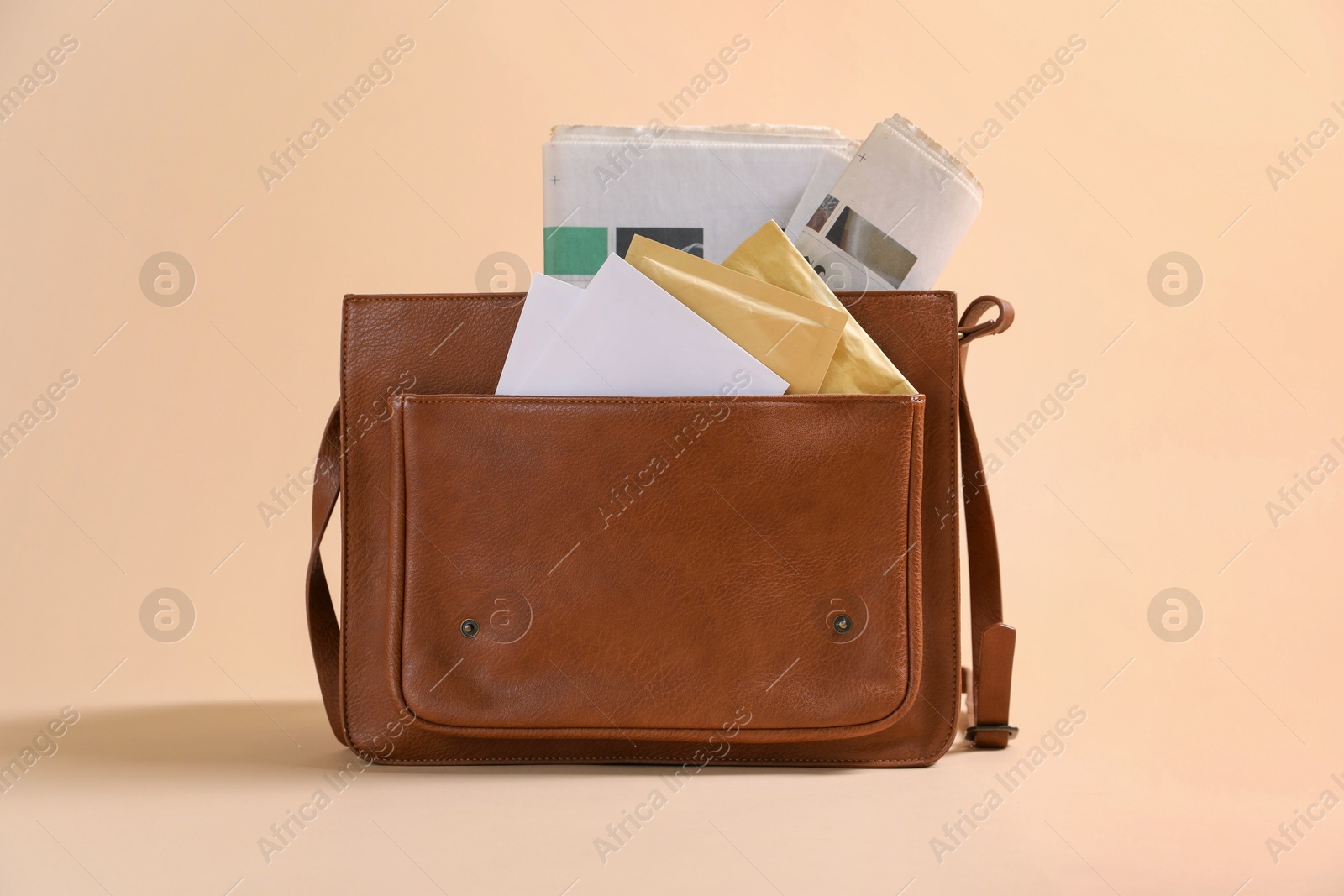 Photo of Brown postman's bag with envelopes and newspapers on beige background