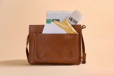 Photo of Brown postman's bag with envelopes and newspapers on beige background