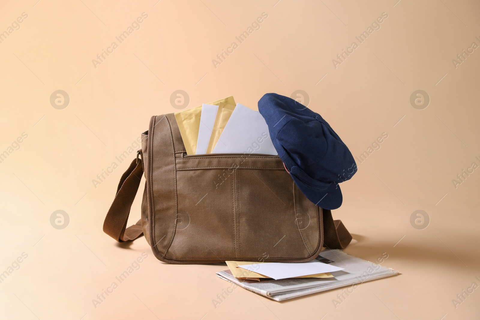 Photo of Brown postman's bag, envelopes, newspapers and hat on beige background