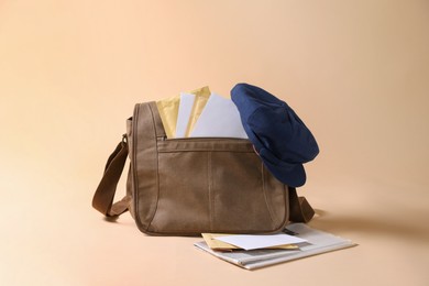 Brown postman's bag, envelopes, newspapers and hat on beige background