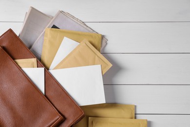 Brown postman's bag with envelopes and newspapers on white wooden table, top view. Space for text