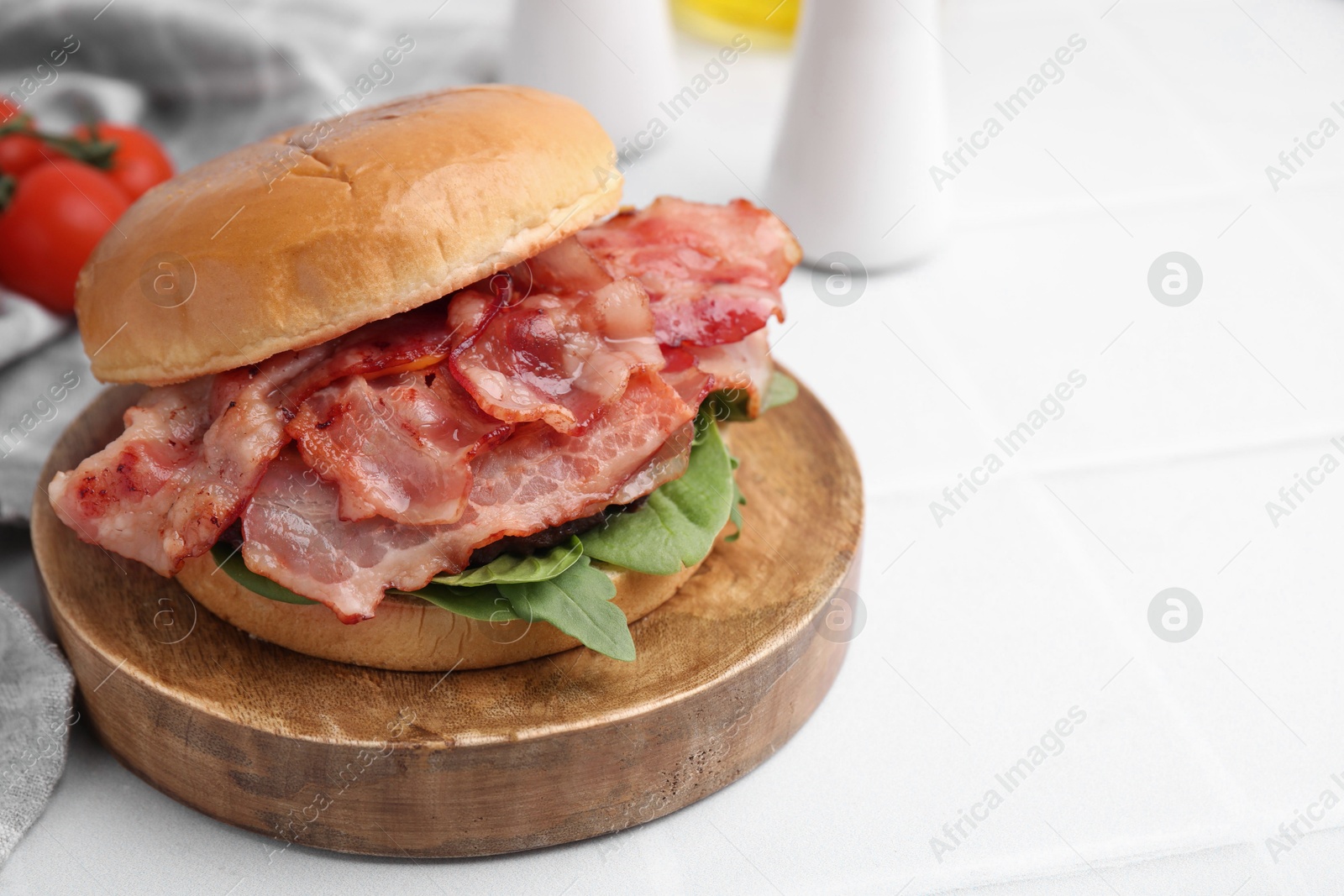 Photo of Delicious burger with bacon and greens on white tiled table, closeup. Space for text