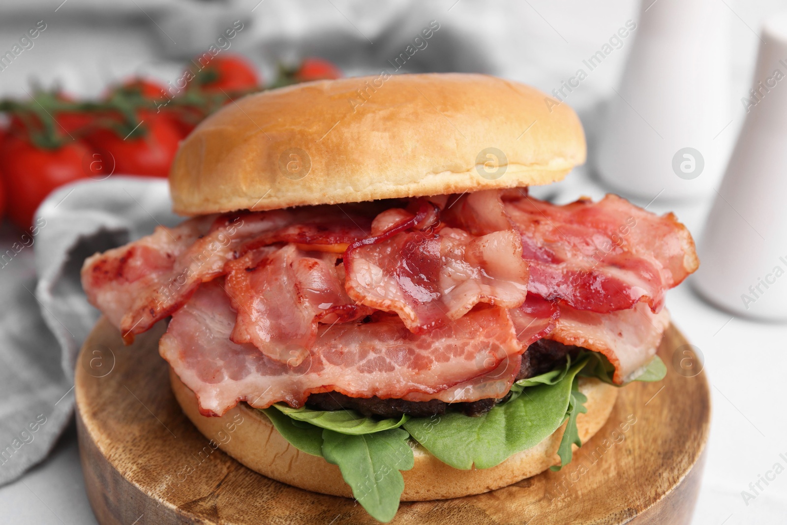 Photo of Delicious burger with bacon and greens on table, closeup