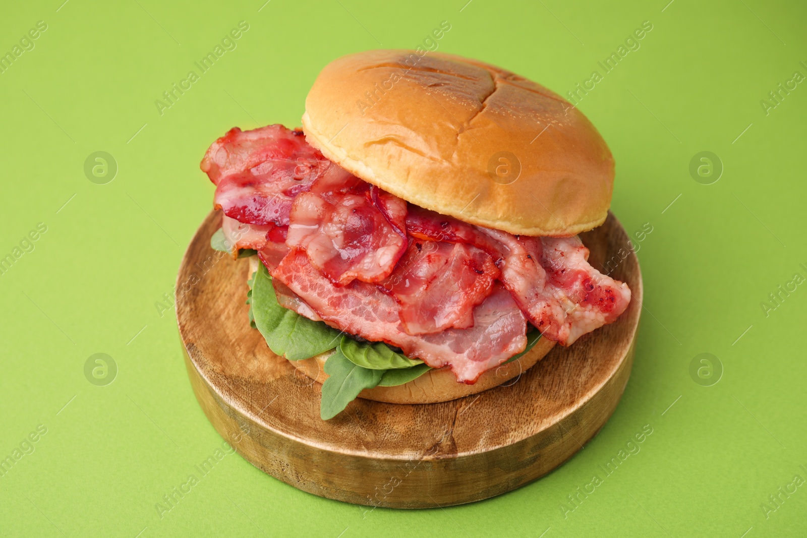 Photo of Delicious burger with bacon and greens on green table, closeup