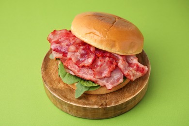 Photo of Delicious burger with bacon and greens on green table, closeup