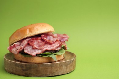 Photo of Delicious burger with bacon and greens on green background, space for text