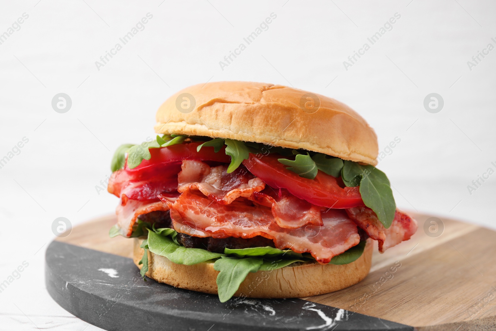 Photo of Delicious burger with bacon, tomato and greens on light background, closeup