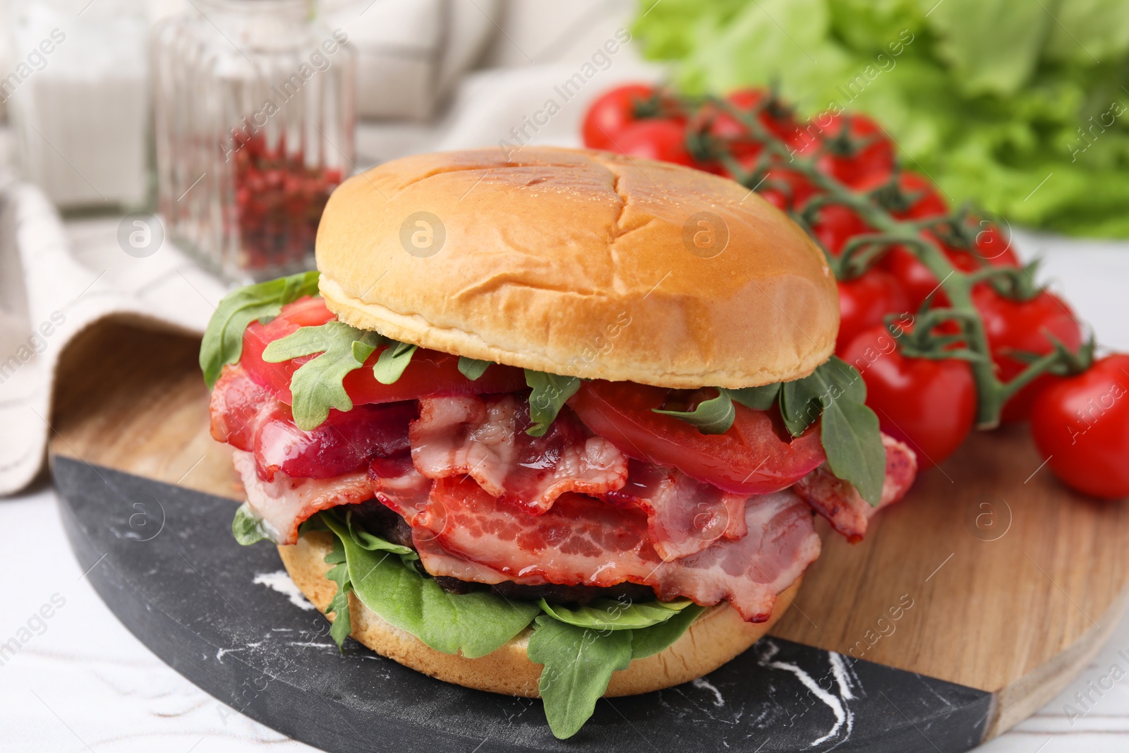 Photo of Delicious burger with bacon, tomato and greens on light table, closeup