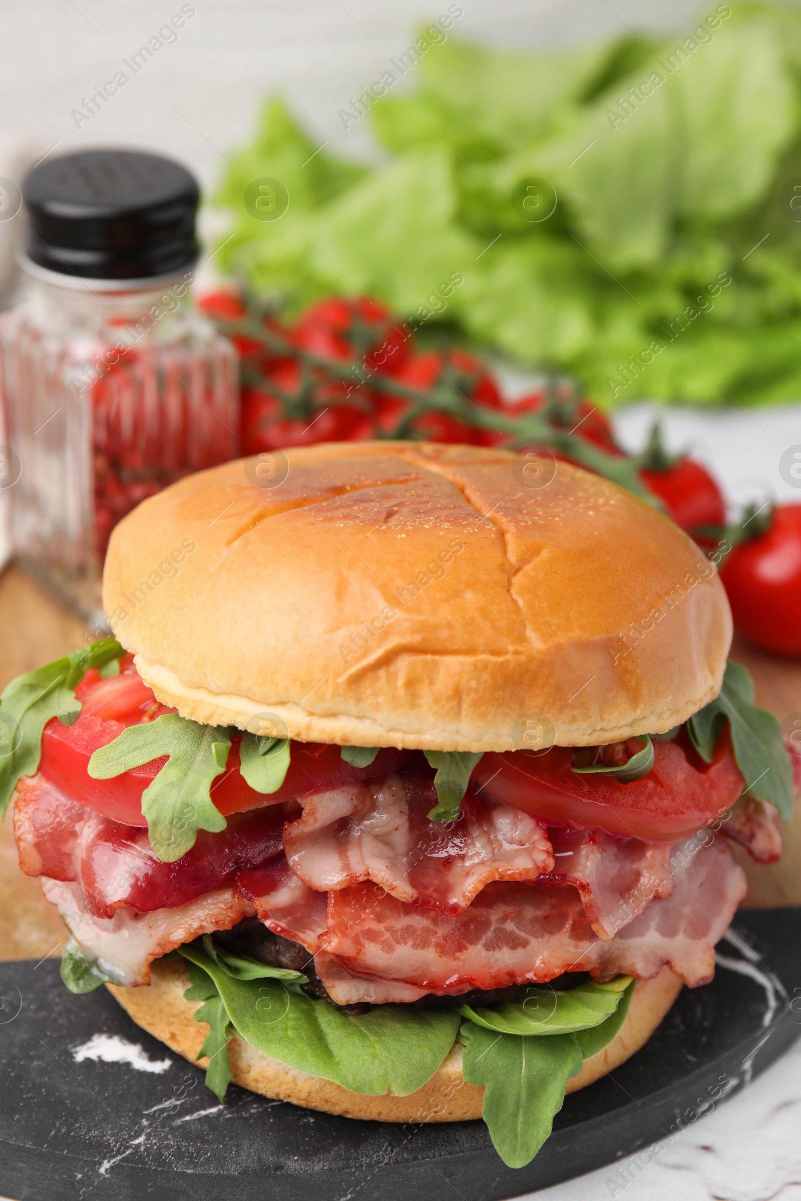 Photo of Delicious burger with bacon, tomato and greens on table, closeup