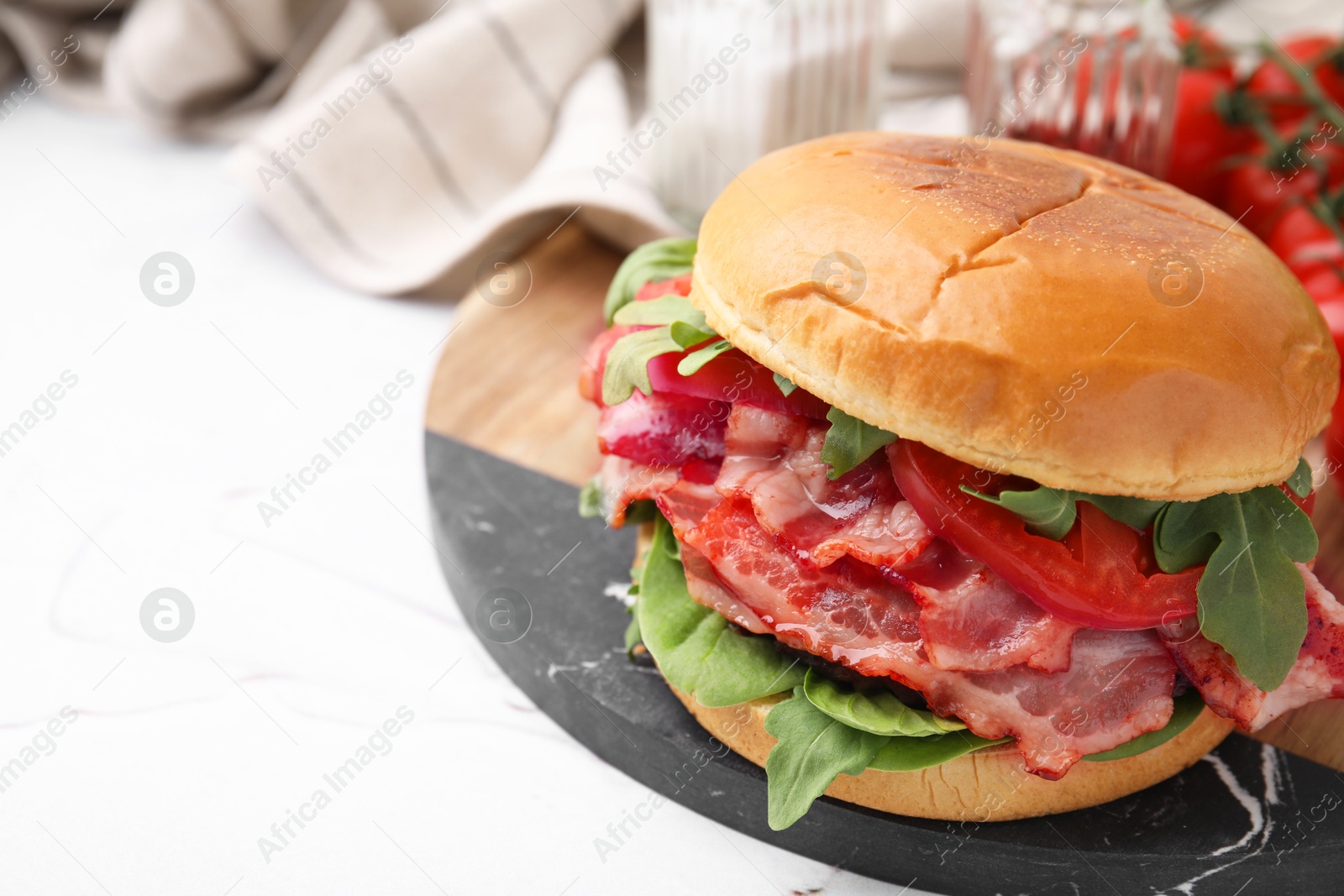 Photo of Delicious burger with bacon, tomato and greens on light textured table, closeup. Space for text