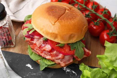 Photo of Delicious burger with bacon, tomato and greens on table, closeup