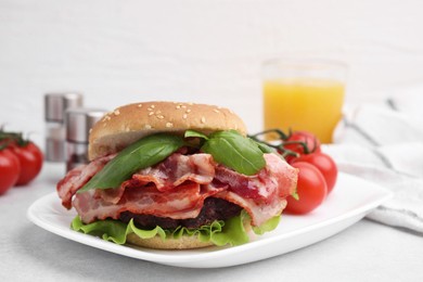 Photo of Delicious burger with bacon and greens on light table, closeup