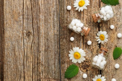 Photo of Homeopathic remedy. Flat lay composition with many pills, bottles and chamomile flowers on wooden table, space for text