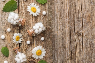 Homeopathic remedy. Flat lay composition with many pills, bottles and chamomile flowers on wooden table, space for text